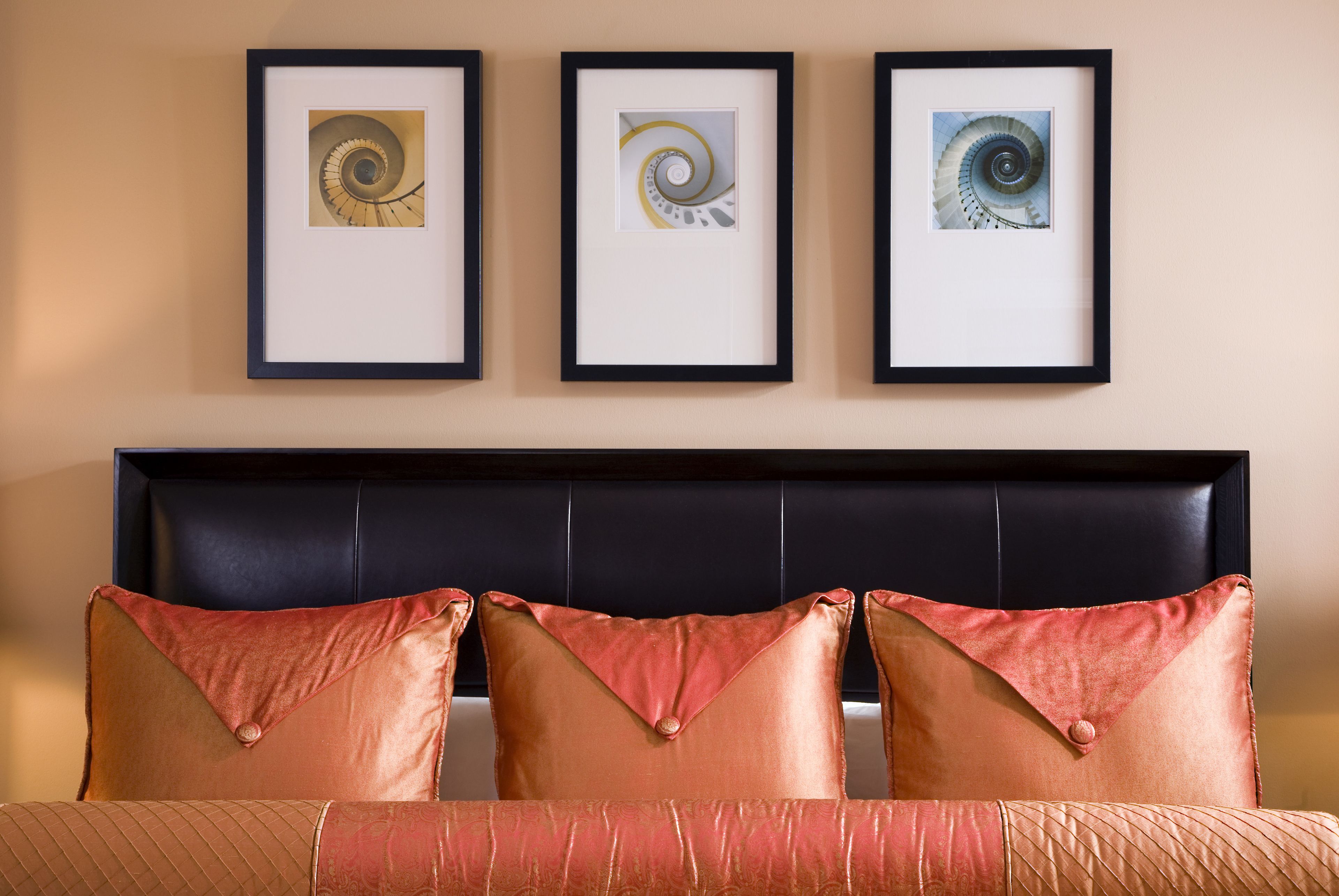 A bed with three pillows and three framed pictures of a spiral staircase on the wall above.