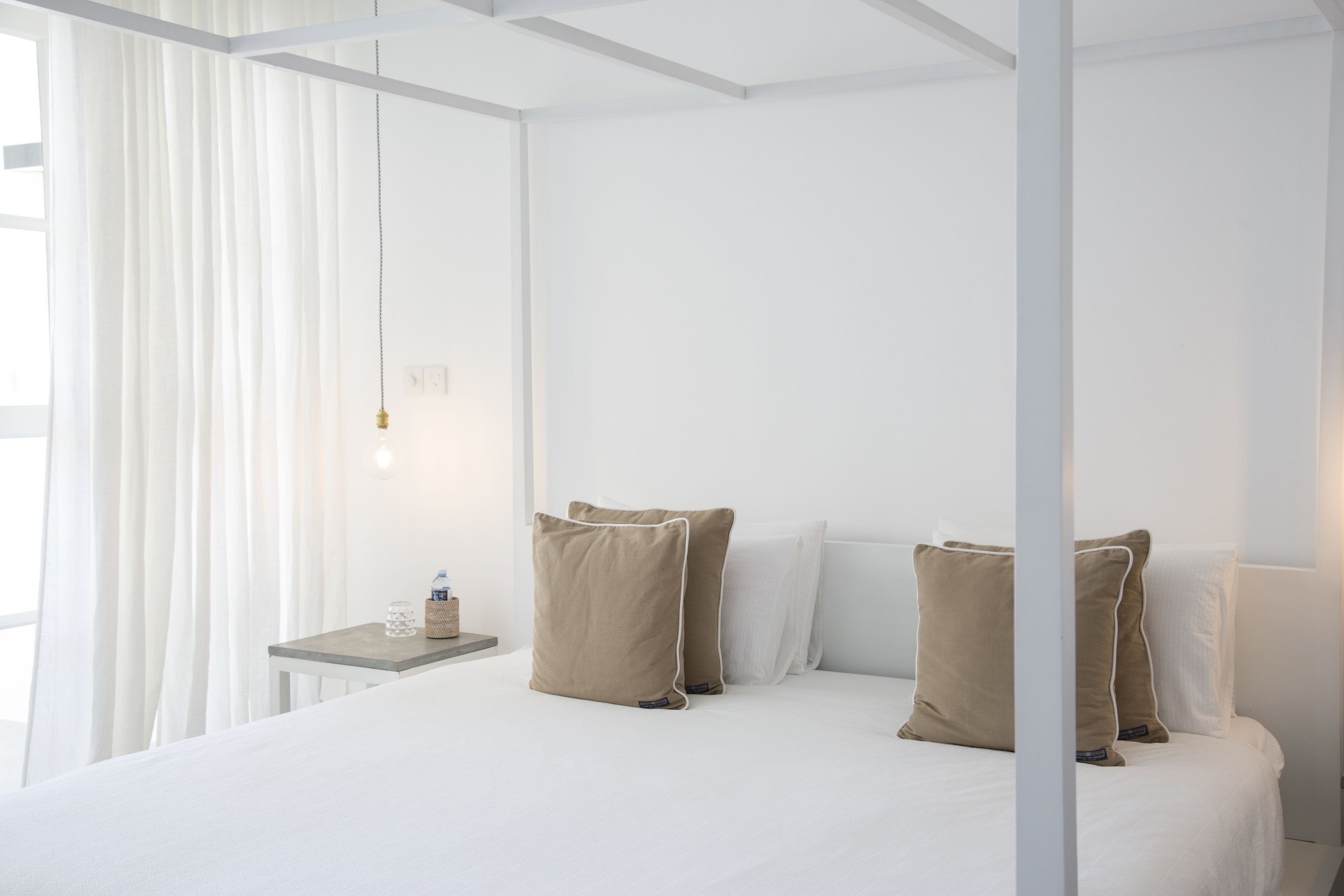 Une chambre d’hôtel avec un lit à baldaquin, des murs blancs et une petite table de chevet avec une lampe.