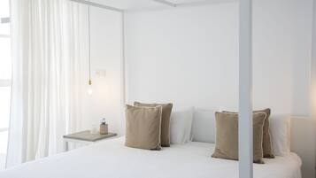 Une chambre d’hôtel avec un lit à baldaquin, des murs blancs et une petite table de chevet avec une lampe.