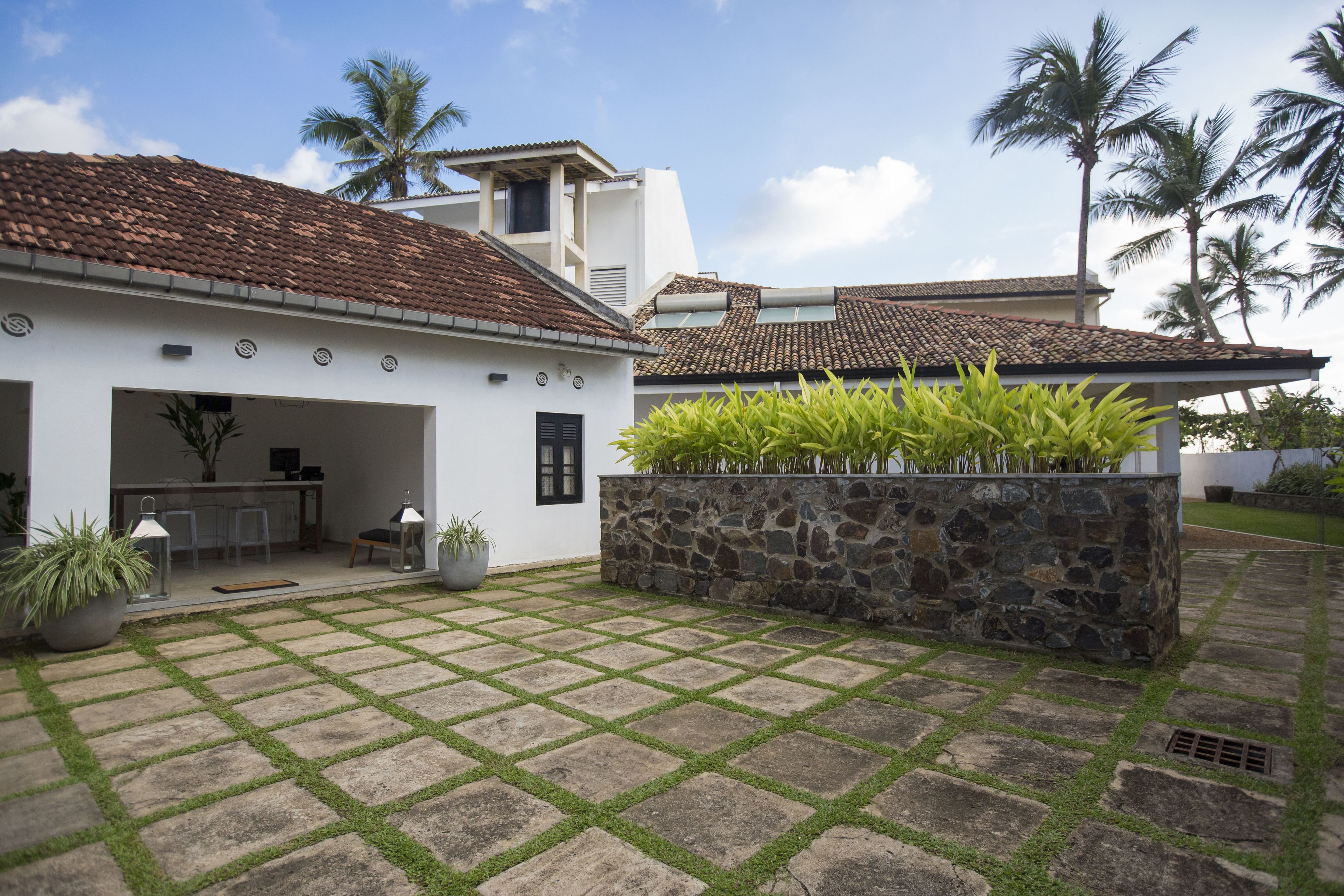 A courtyard with a tiled roof, stone planter with plants, and a white building with a kitchen area visible.