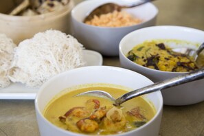 Eine Schüssel Suppe mit Löffel, ein Teller mit weißen Nudeln und zwei Curry-Schüsseln.