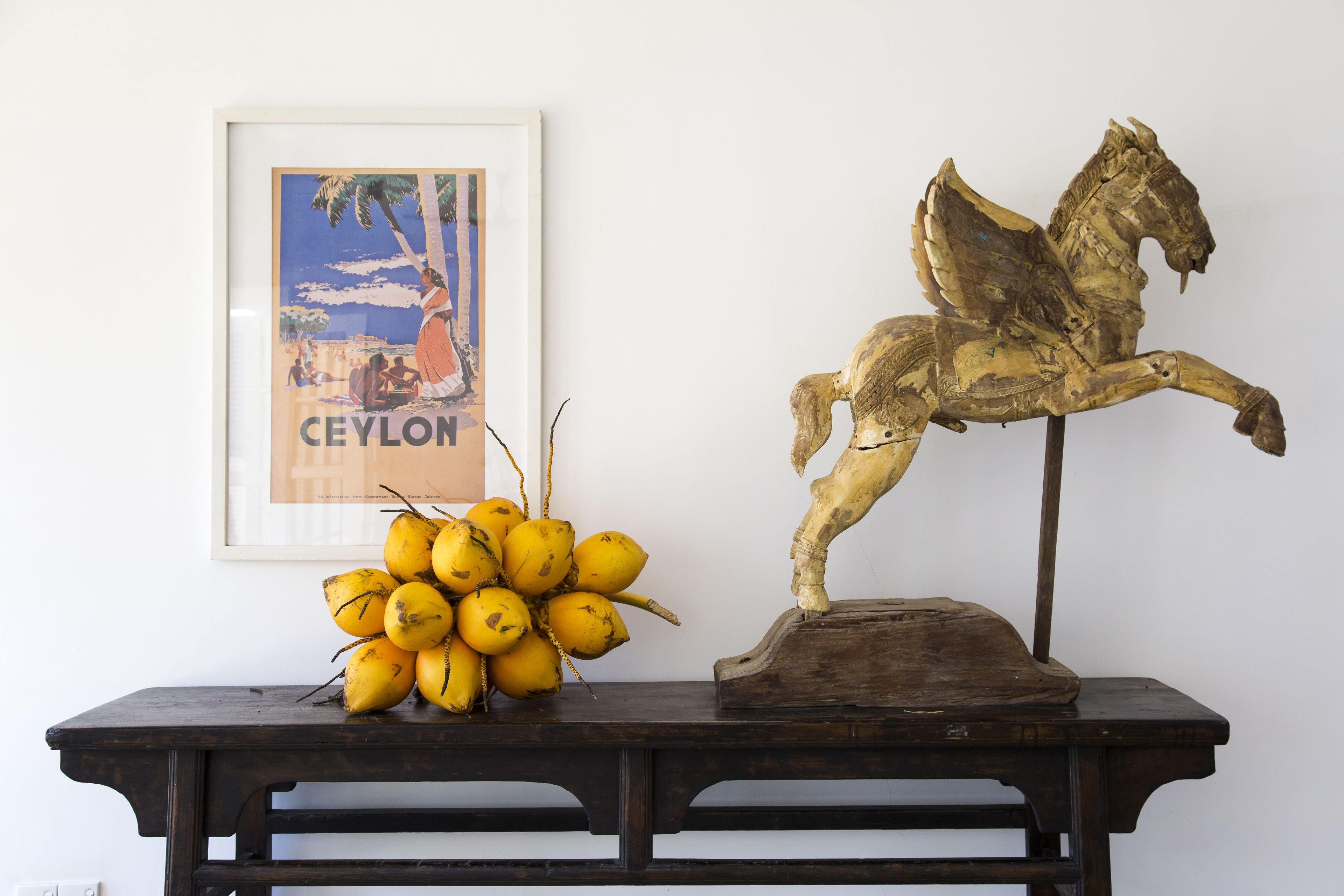 Une table sur laquelle on voit un assortiment de fruits jaunes et une sculpture équestre en bois.