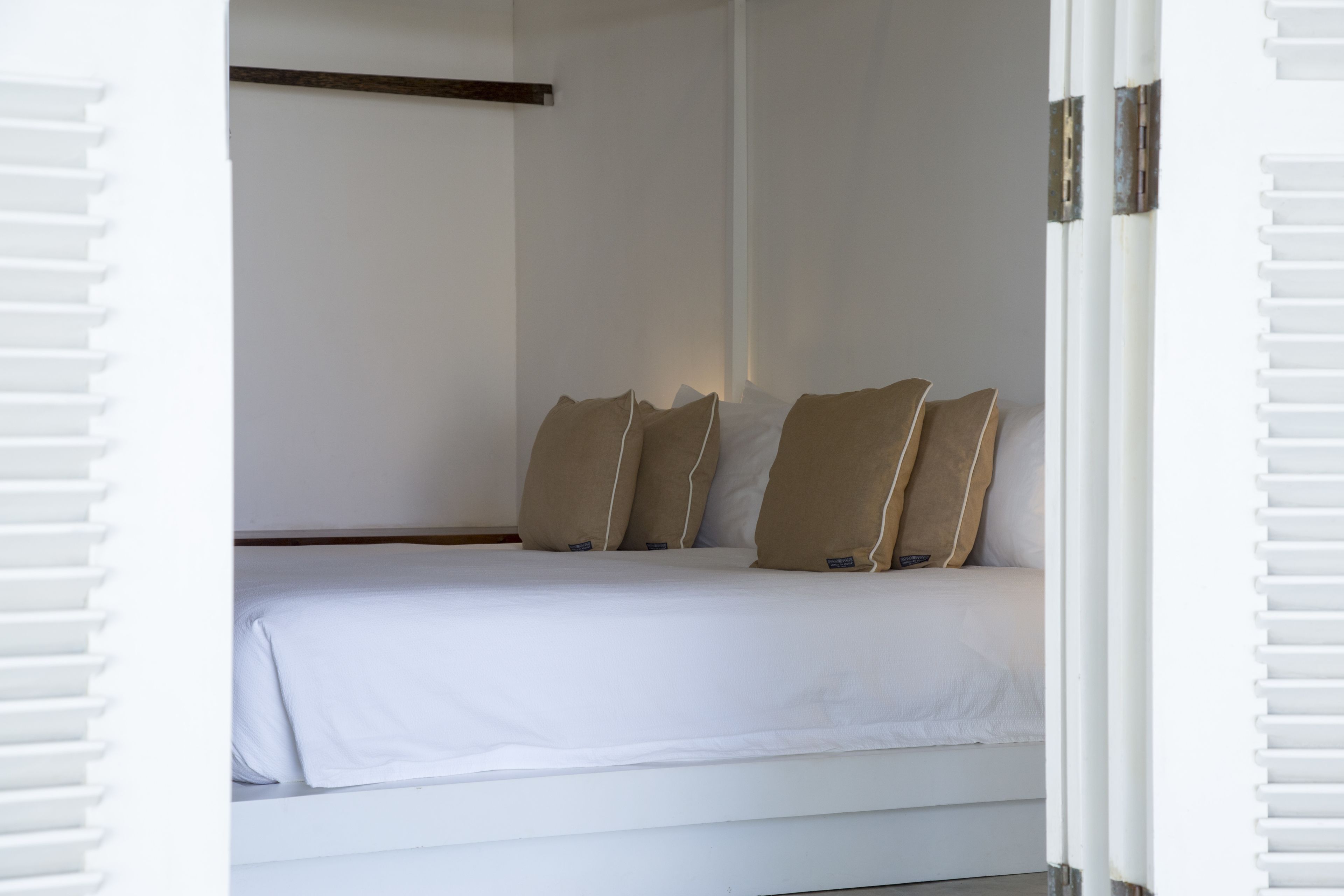 Un dormitorio con cama, ropa de cama blanca y almohadas color beige.