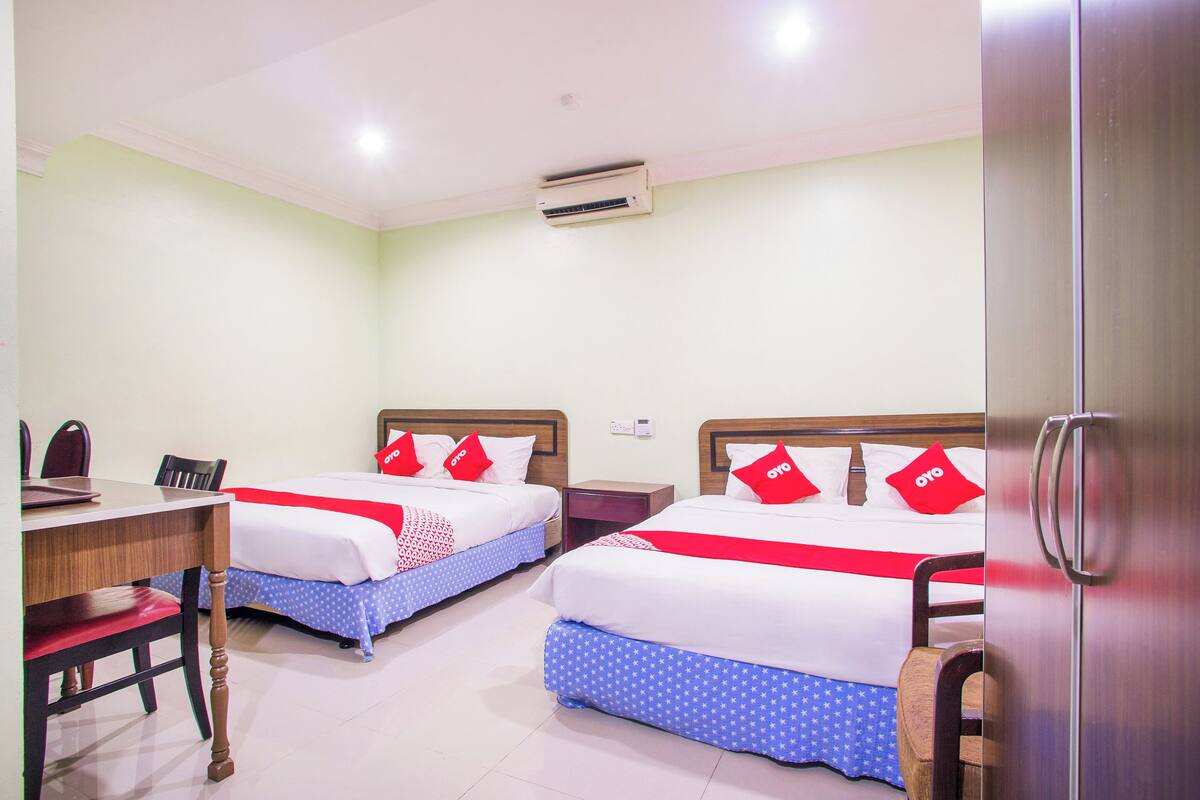 A hotel room with two beds, a desk, chairs, and a wardrobe.