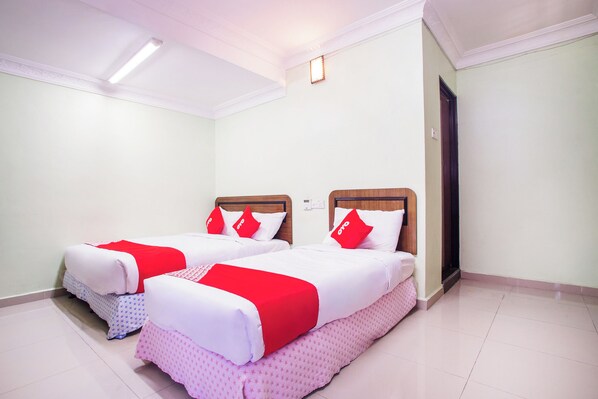 A hotel room with two beds, each with a wooden headboard, white bedding, and red pillows.