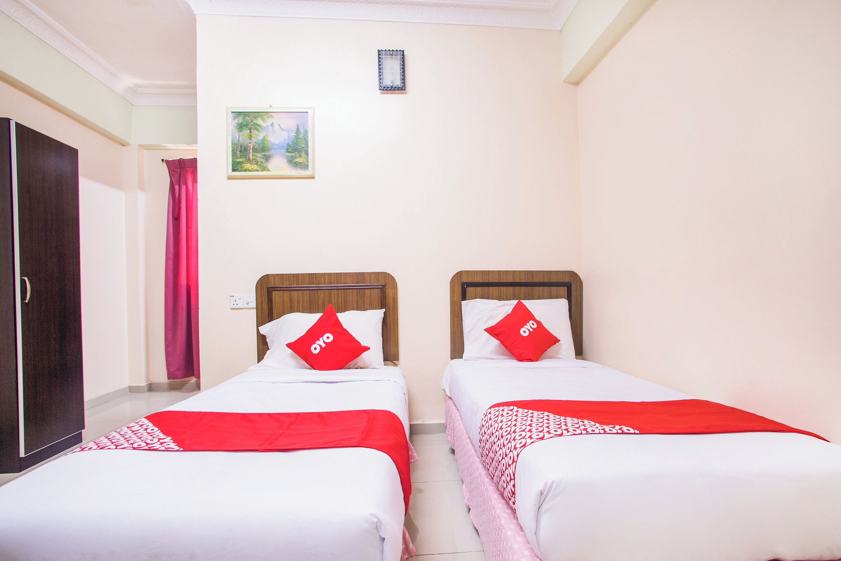 A hotel room with two single beds, each with a red pillow and a white bedspread.