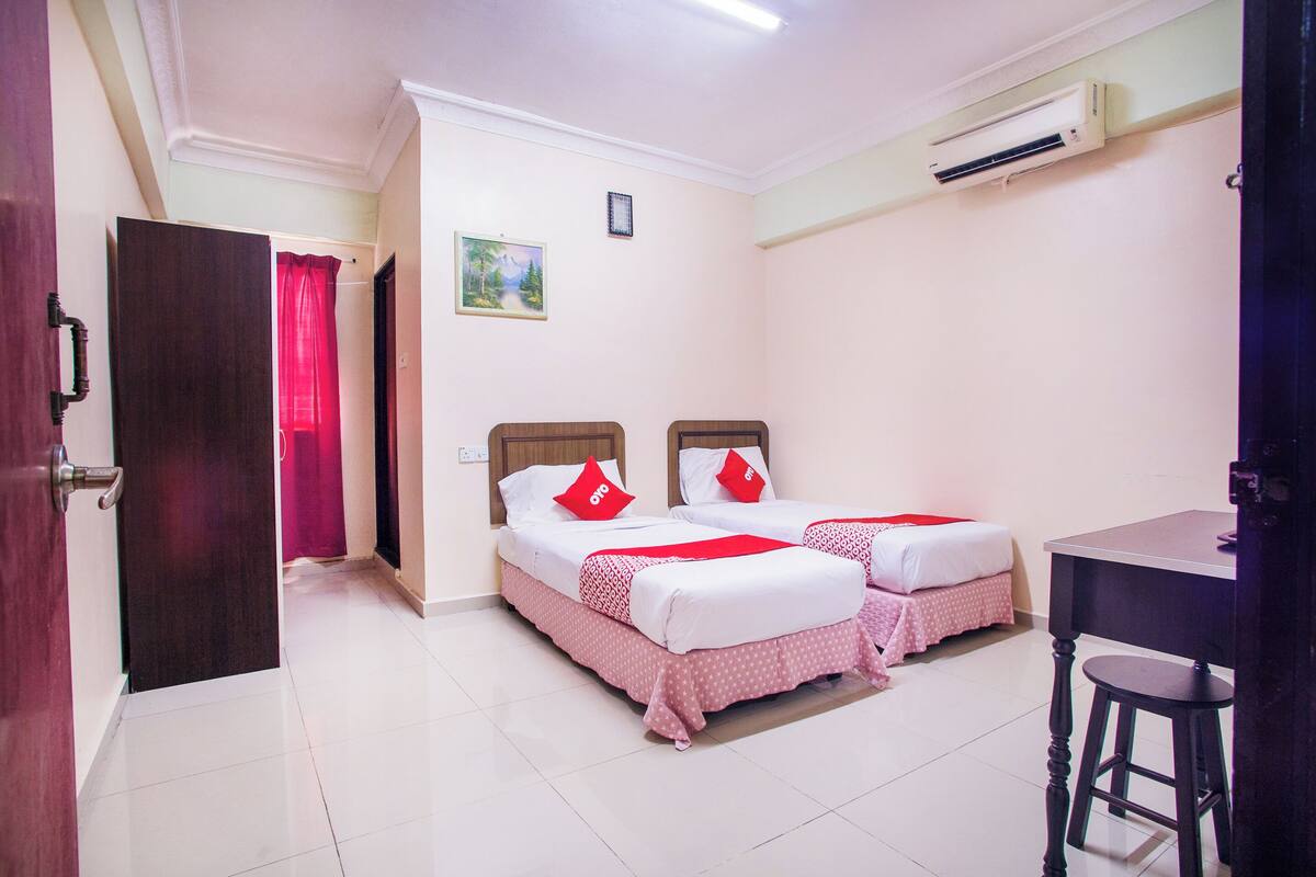 A hotel room with two beds, a desk, and an air conditioning unit.