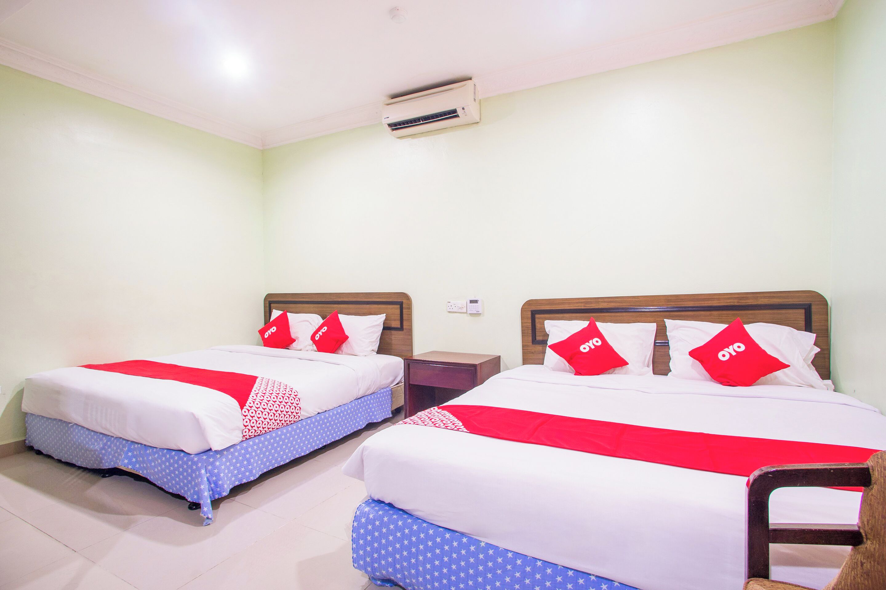 Two beds with red and white bedding, a wooden headboard, and a small wooden nightstand between them.