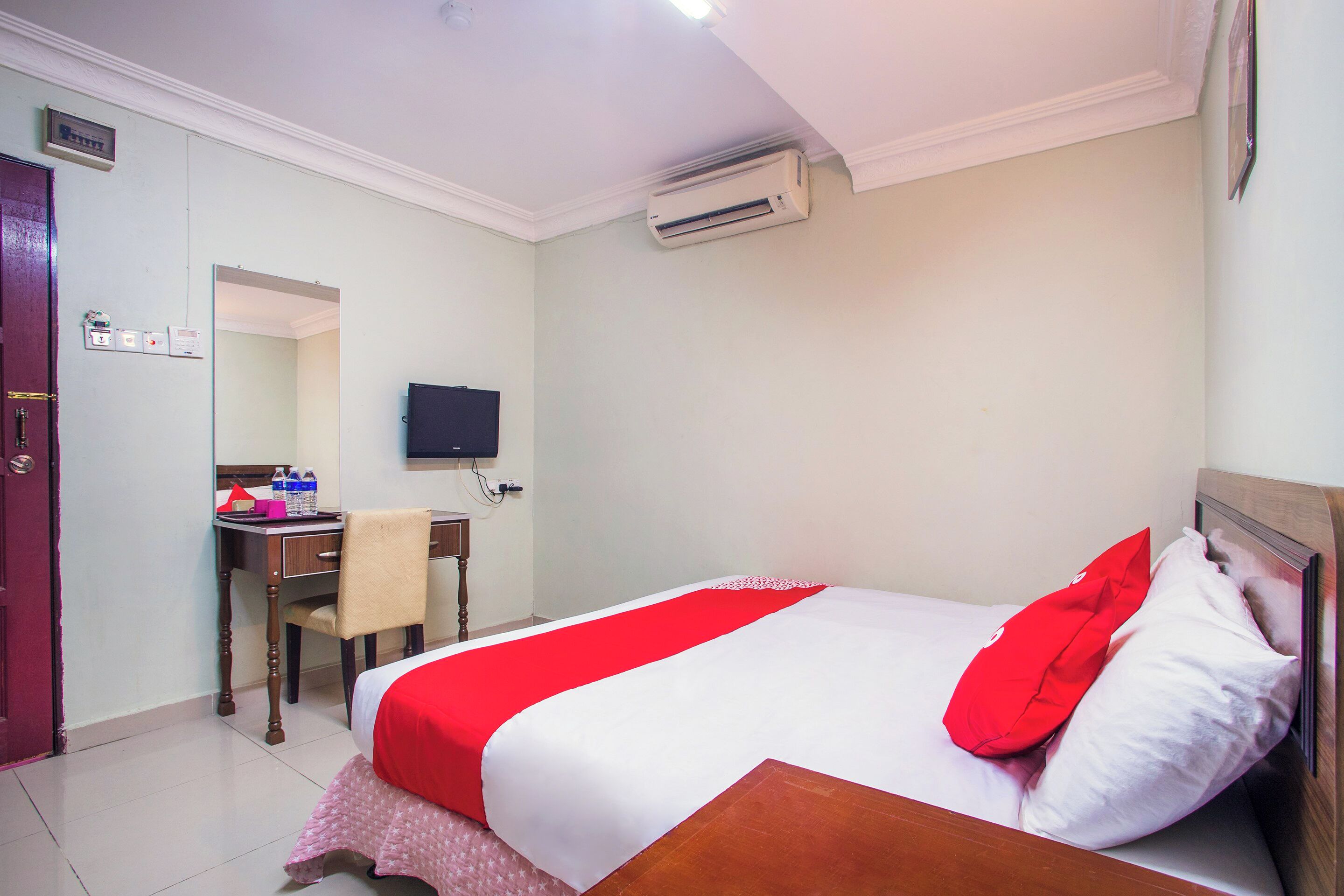 A hotel room with a bed, a desk, a chair, an air conditioner, and a television.