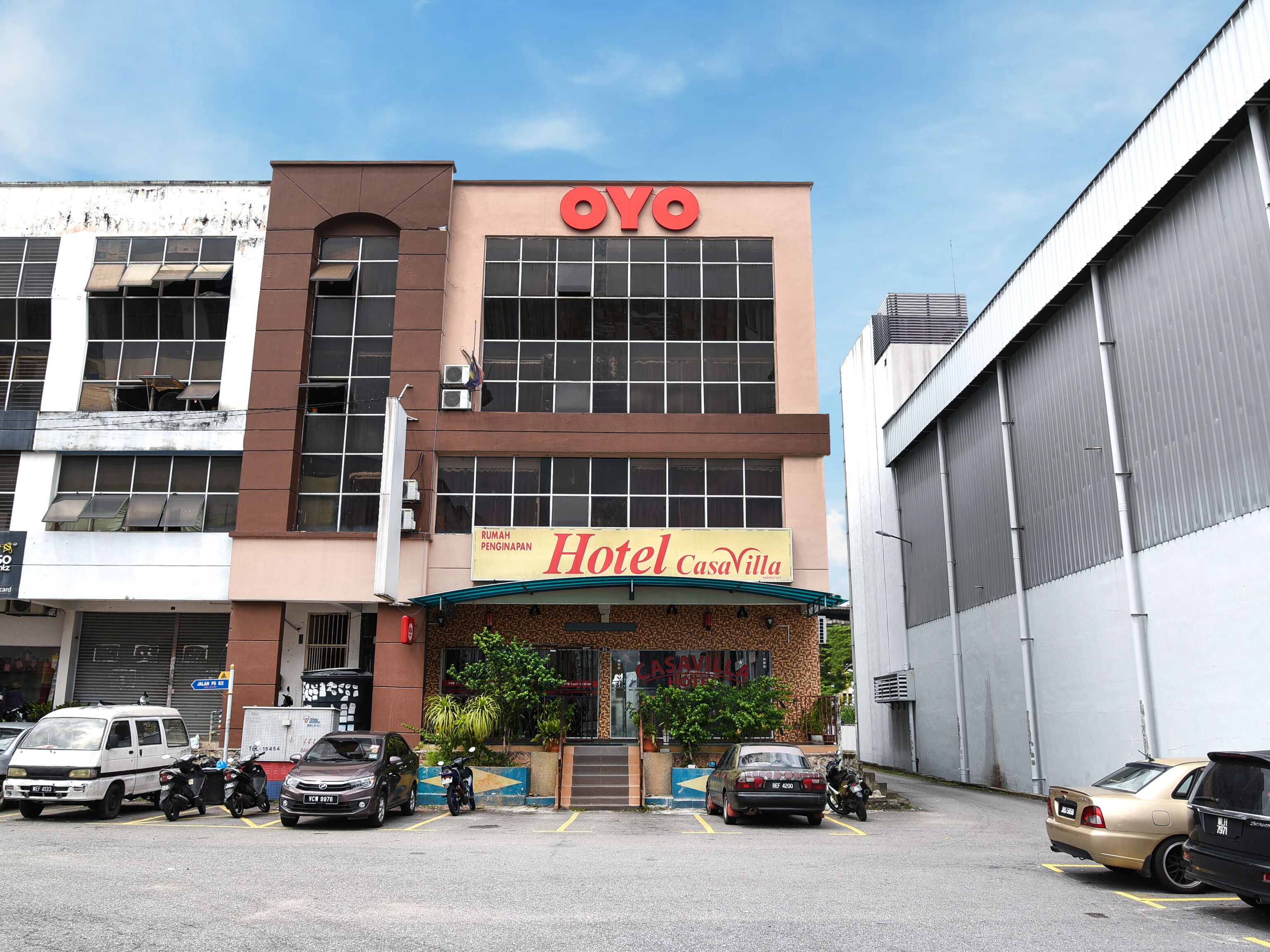 A building with a 'Hotel CasaVilla' sign, a 'OYO' sign above, and a parking area with several vehicles.