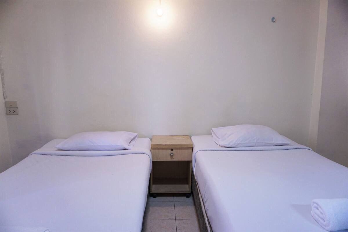 A twin room with two single beds, a wooden nightstand between them, and a light fixture above.