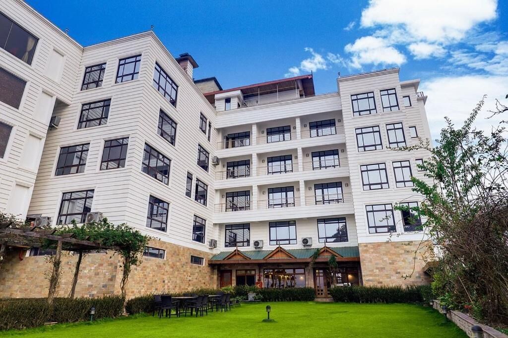 Hotel de vários andares com um pátio, mobiliado com mesas ao ar livre, e um pequeno edifício com telhado verde.