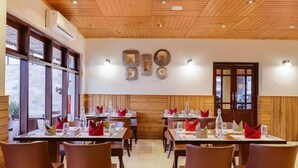 Ein Restaurant mit Holzbalkendecke und -wänden, Tischen mit roten Servietten und großen Fenstern.