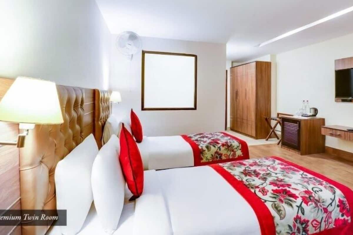 Ein Hotelzimmer mit zwei Betten, einem Fernseher, einem Schreibtisch und einem Kleiderschrank.