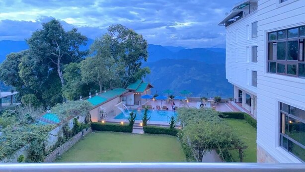 Ein Hotel mit Pool, umgeben von Grün und Bergen im Hintergrund.