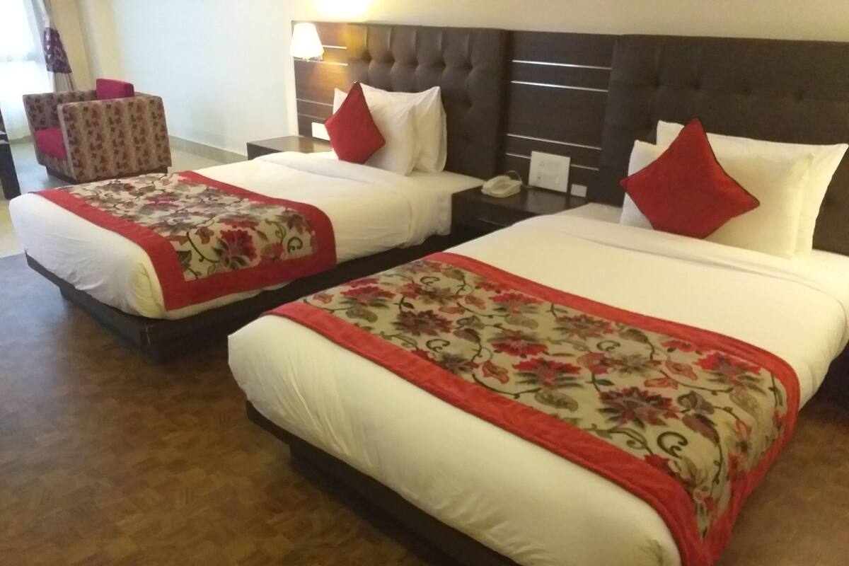 Ein Hotelzimmer mit zwei Betten, jeweils mit einer rot-beigen Blumendecke, einem dunklen Kopfteil und einem Nachttisch mit Lampe und Telefon.
