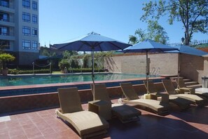 A poolside area with lounge chairs and umbrellas, a brick wall, and a building in the background. - Sobralia Hotels Casino Resort & Spa (Namchi)