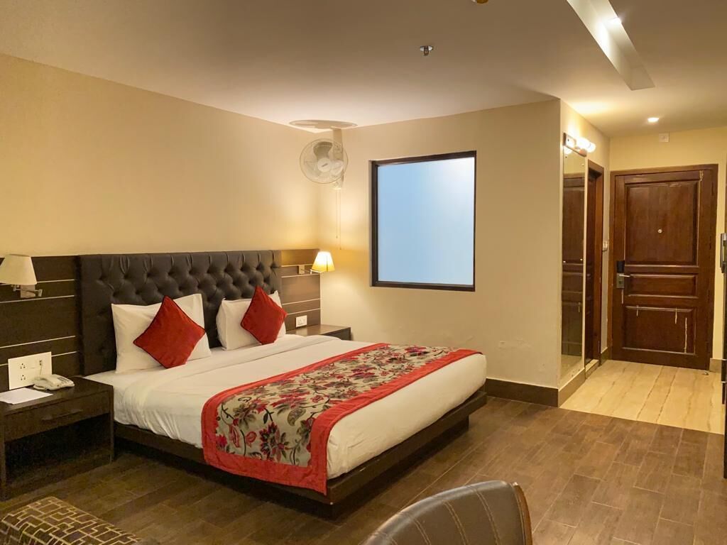 Une chambre d’hôtel avec un grand lit, une table de chevet, un bureau, une chaise, un téléviseur fixé au mur et une porte.