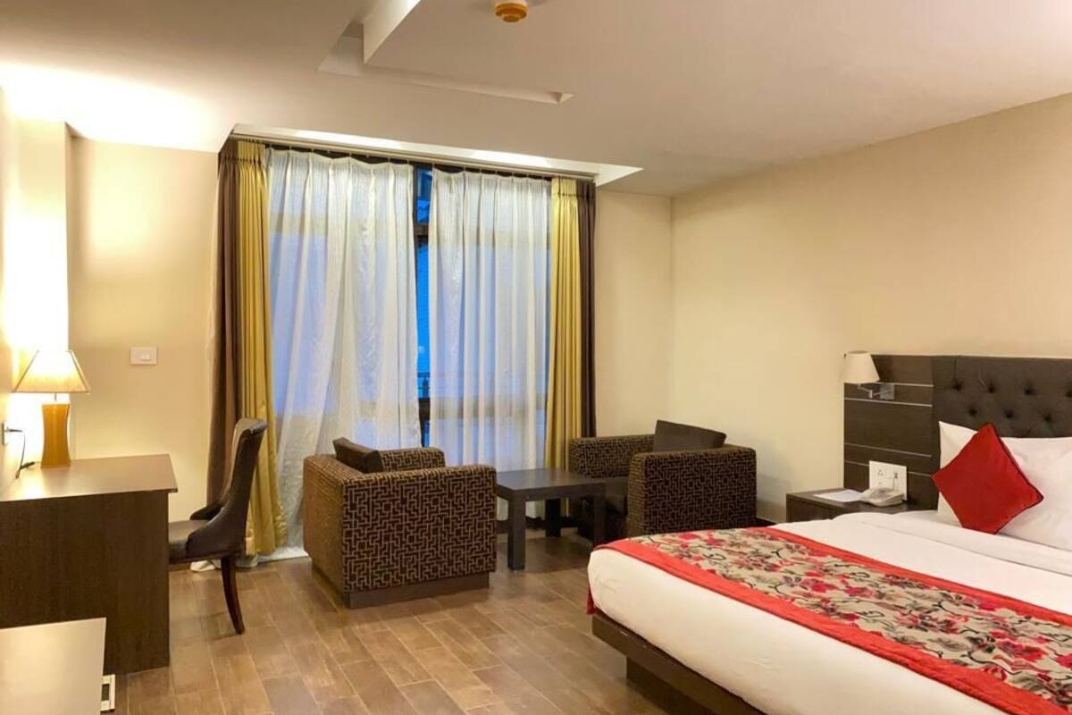 Ein Hotelzimmer mit Bett, Schreibtisch, zwei Stühlen, einem kleinen Tisch und einem Fenster mit Vorhängen.