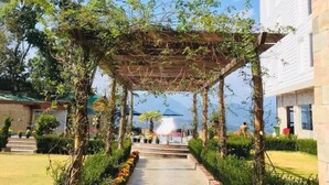 Ein überdachter Weg mit einer Pergola, gesäumt von ordentlich geschnittenen Hecken und Topfpflanzen, der zu einem Gebäude mit weißer Fassade führt.