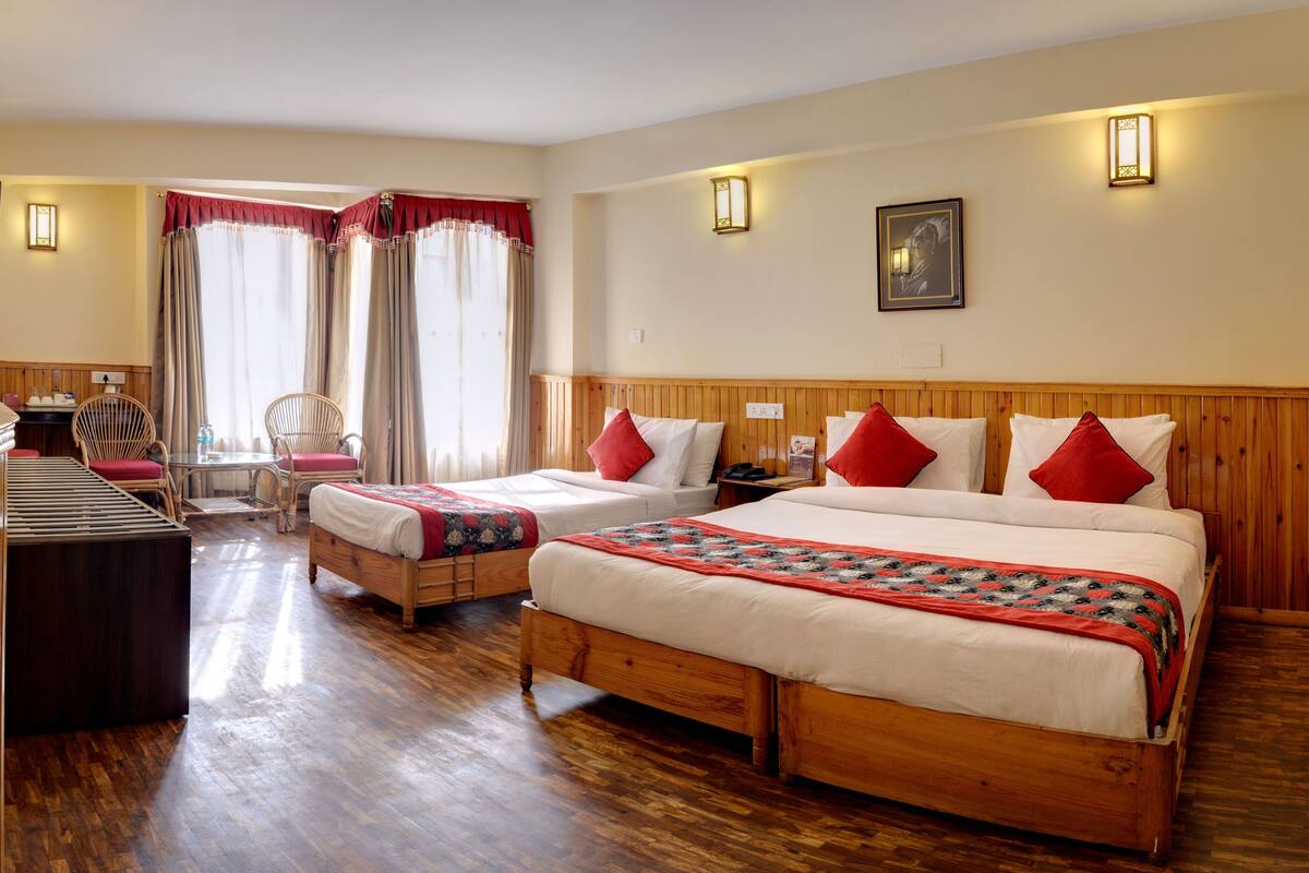 Une chambre d’hôtel avec deux lits, une tête de lit en bois, un bureau avec une chaise et une fenêtre avec des rideaux.