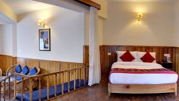 A bedroom with a wooden bed, red and white pillows, a blue and white patterned sofa, and a wooden floor.