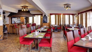 A restaurant with wooden tables, red chairs, and a bar area. - Summit Newa Regency (Gyalshing)
