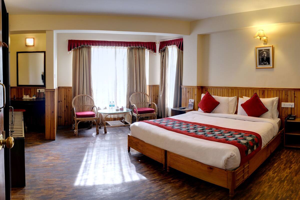 Une chambre d’hôtel avec un lit en bois, deux chaises, une petite table et un bureau avec une lampe.