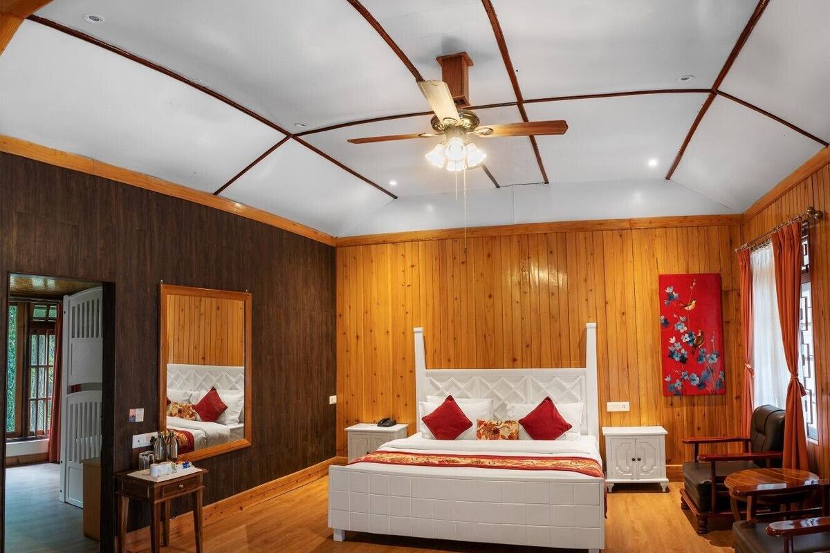 Un dormitorio amplio con una cama grande, suelo de madera, ventilador de techo y paneles de madera en la pared.