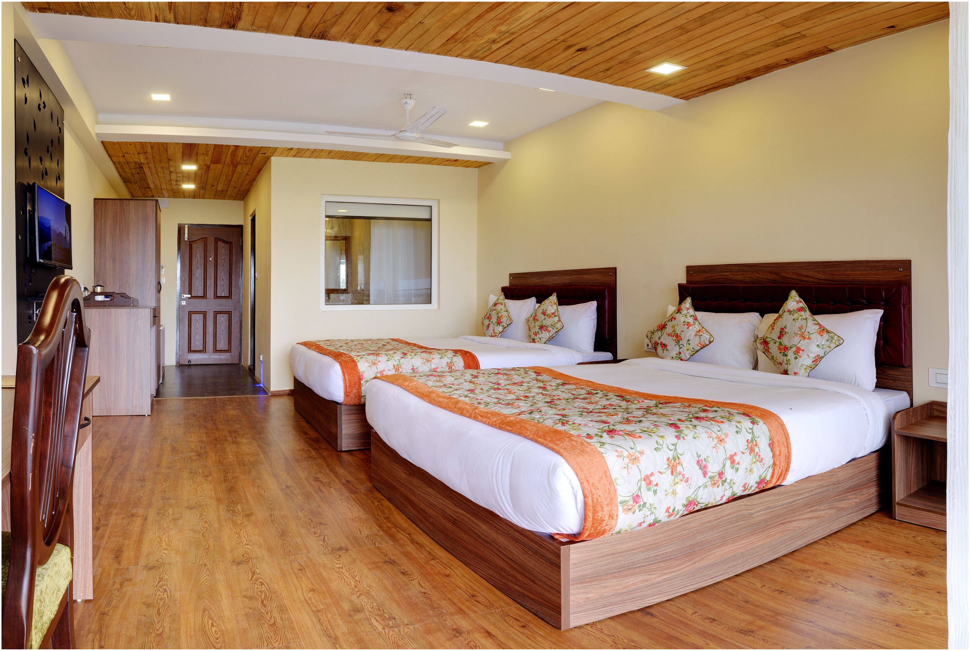 A hotel room with two beds, wooden flooring, a television, and a ceiling fan.