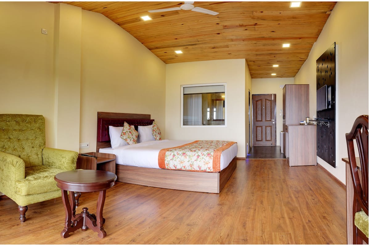 Un dormitorio con cama, techo de madera, ventana, puerta y una mesita.