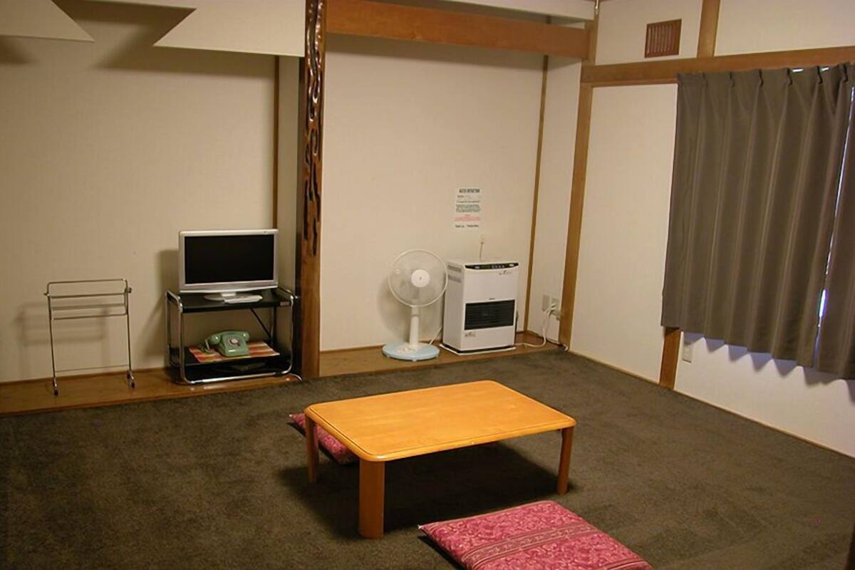 A small room with a wooden table, a television on a stand, a fan, and a heater.