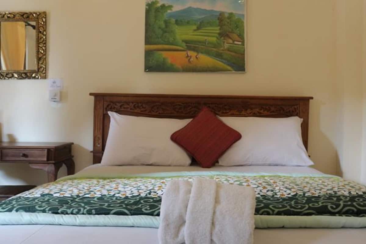 Un dormitorio con cabecera de madera, dos almohadas, colcha y un cuadro de un paisaje en la pared.