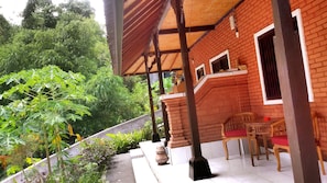 A covered outdoor area with a brick wall, a wooden chair, and a table. - Karma House Ubud (Ubud)
