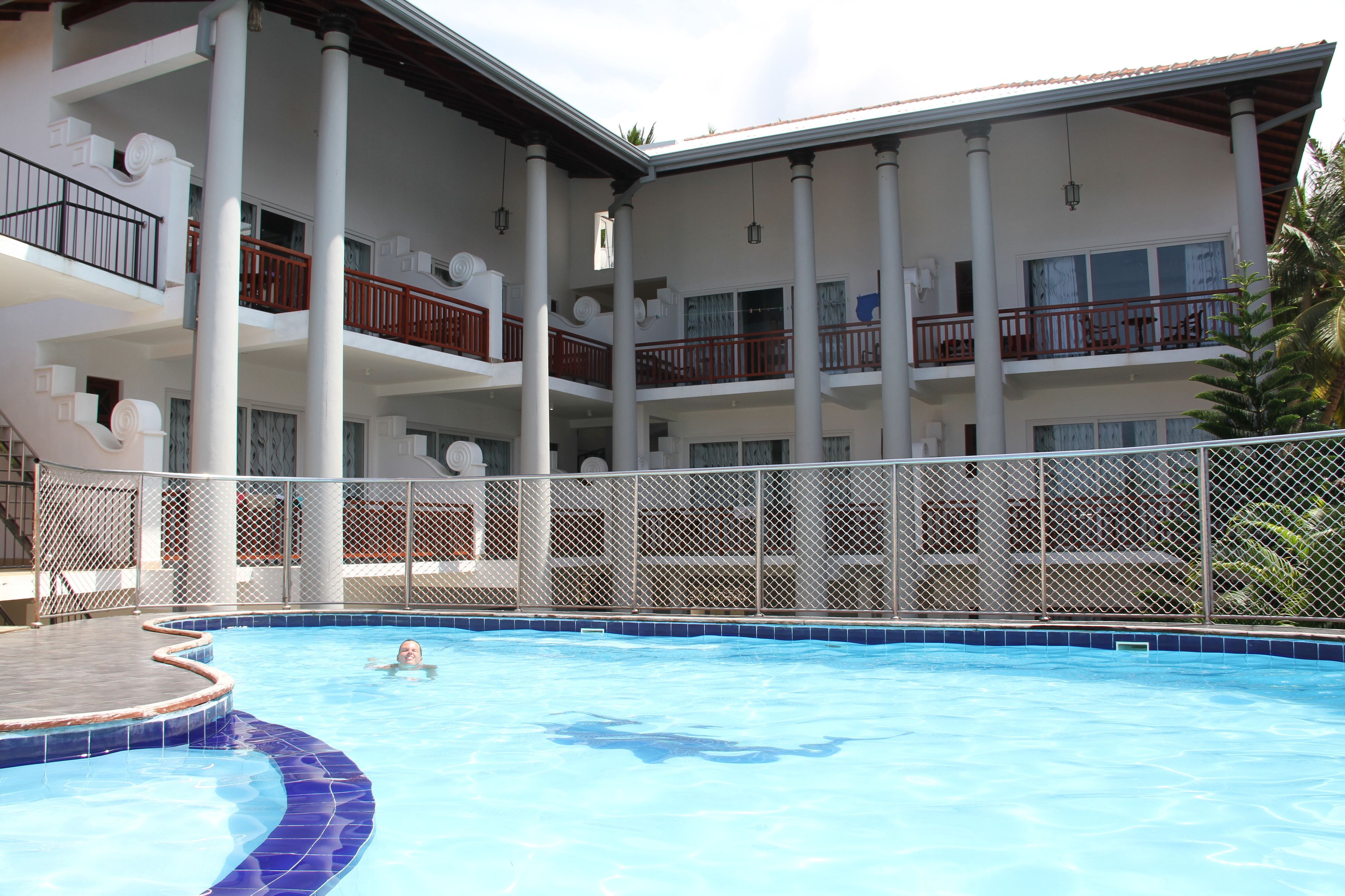 A swimming pool with a person in the water, surrounded by a multi-story building with balconies and railings.