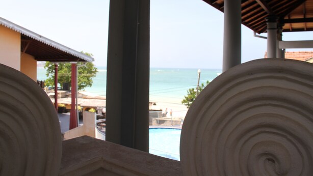 A view of a beach with a pool and a building with a tiled roof. - Neptune Bay Hotel (Unawatuna)