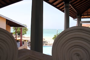 A view of a beach with a pool and a building with a tiled roof. - Neptune Bay Hotel (Unawatuna)