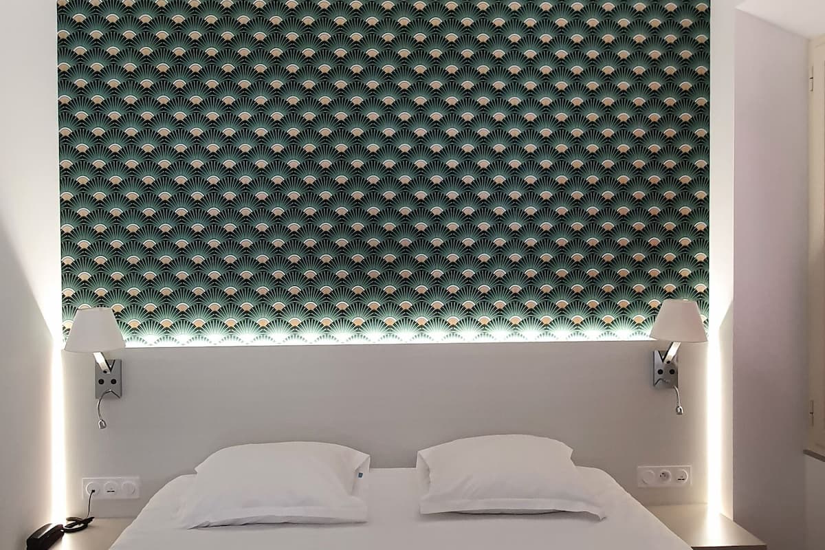Una habitación de hotel con una cama grande, dos lámparas de noche, un teléfono y un cabecero con un diseño estampado en verde.