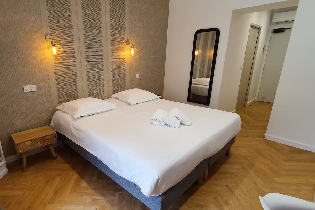 Un dormitorio ordenado con cama, lámparas de noche, un espejo y un banco de madera.