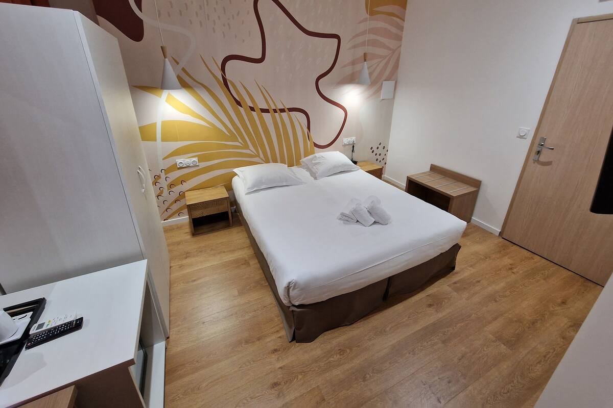 Una habitación de hotel con cama, mesitas de noche, armario y una pared con diseño de hojas.