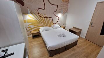 A hotel room with a bed, bedside tables, a wardrobe, and a wall with a leaf pattern.