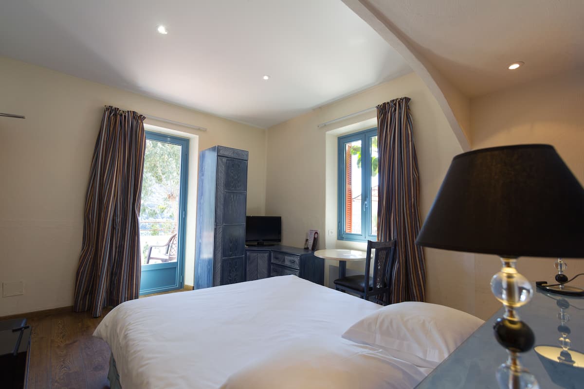 Habitación de hotel con cama, escritorio, silla, televisión y ventana con cortinas.