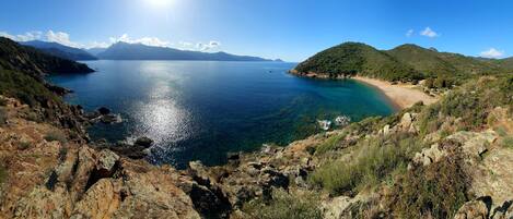 A coastal landscape with a clear view of the sea, rocky terrain, and a small beach area.