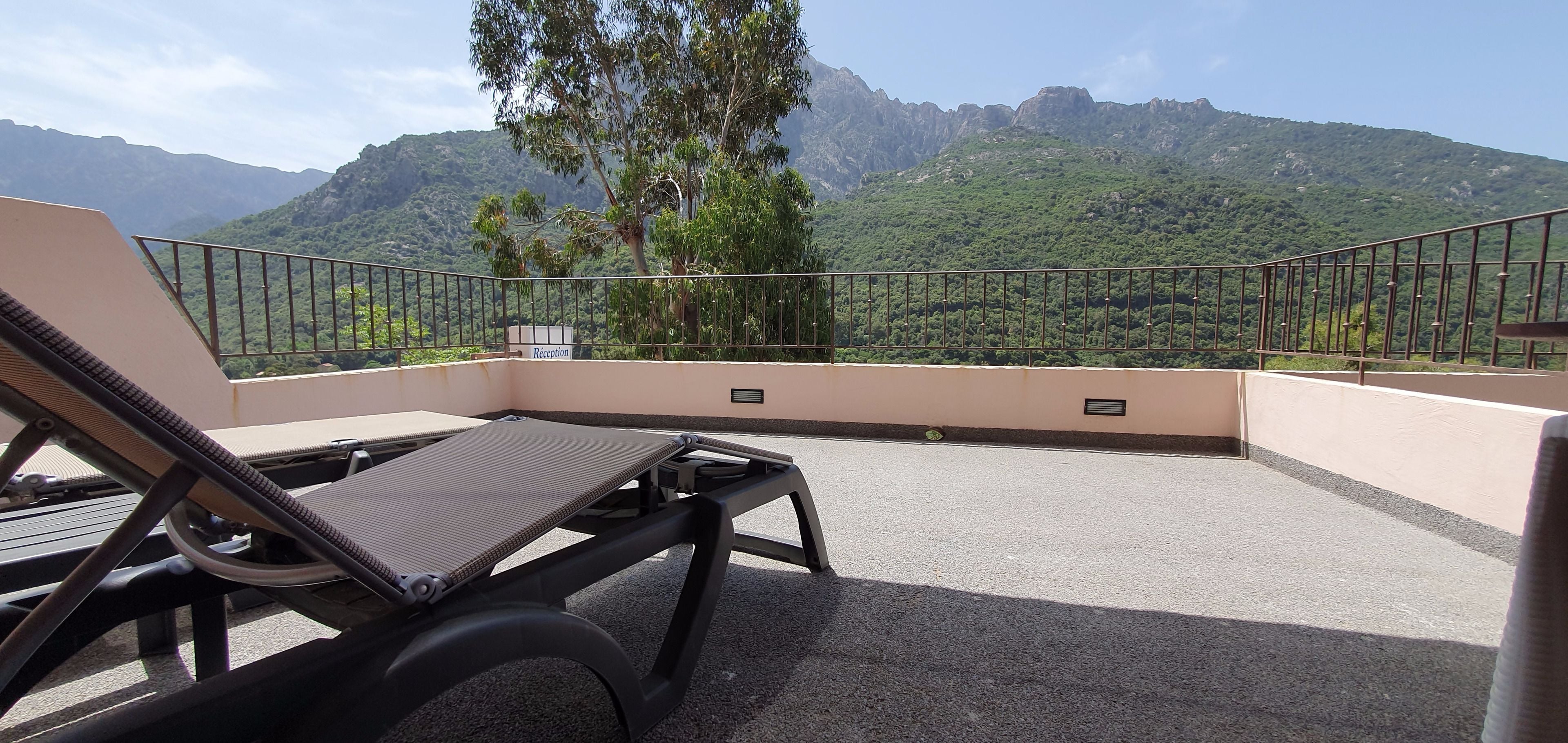 Un balcón con vistas a montañas, un letrero de recepción y una tumbona.