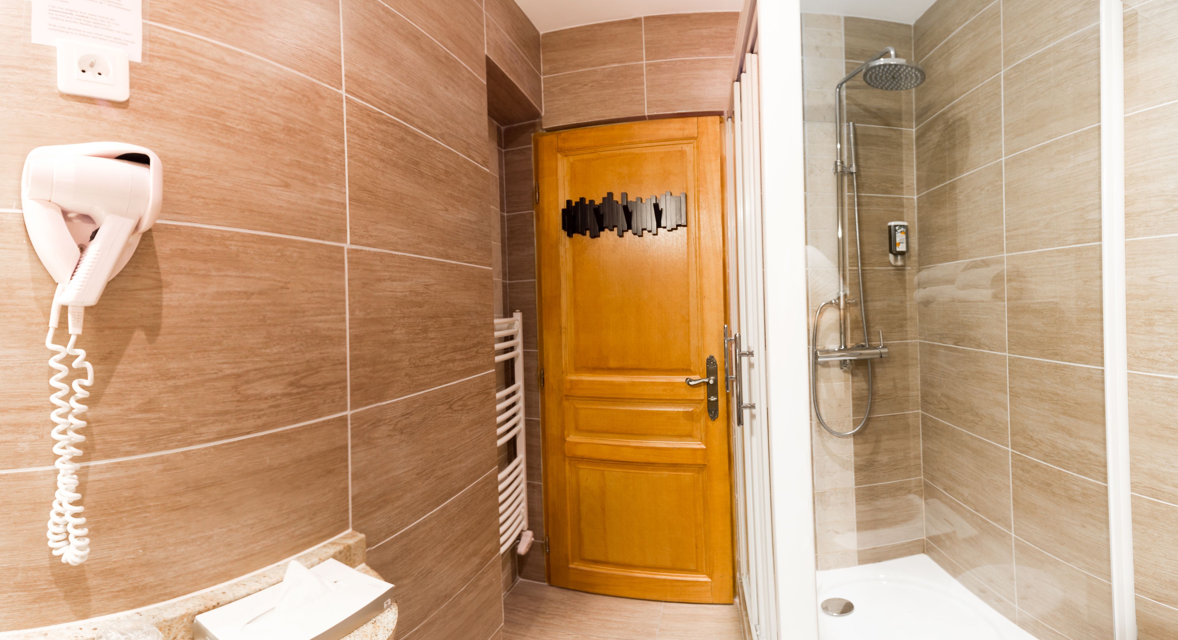 Une salle de bain avec une porte en bois, un sèche-cheveux fixé au mur et un espace douche.