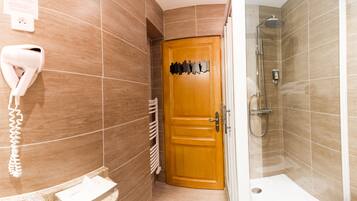 Une salle de bain avec une porte en bois, un sèche-cheveux fixé au mur et un espace douche.