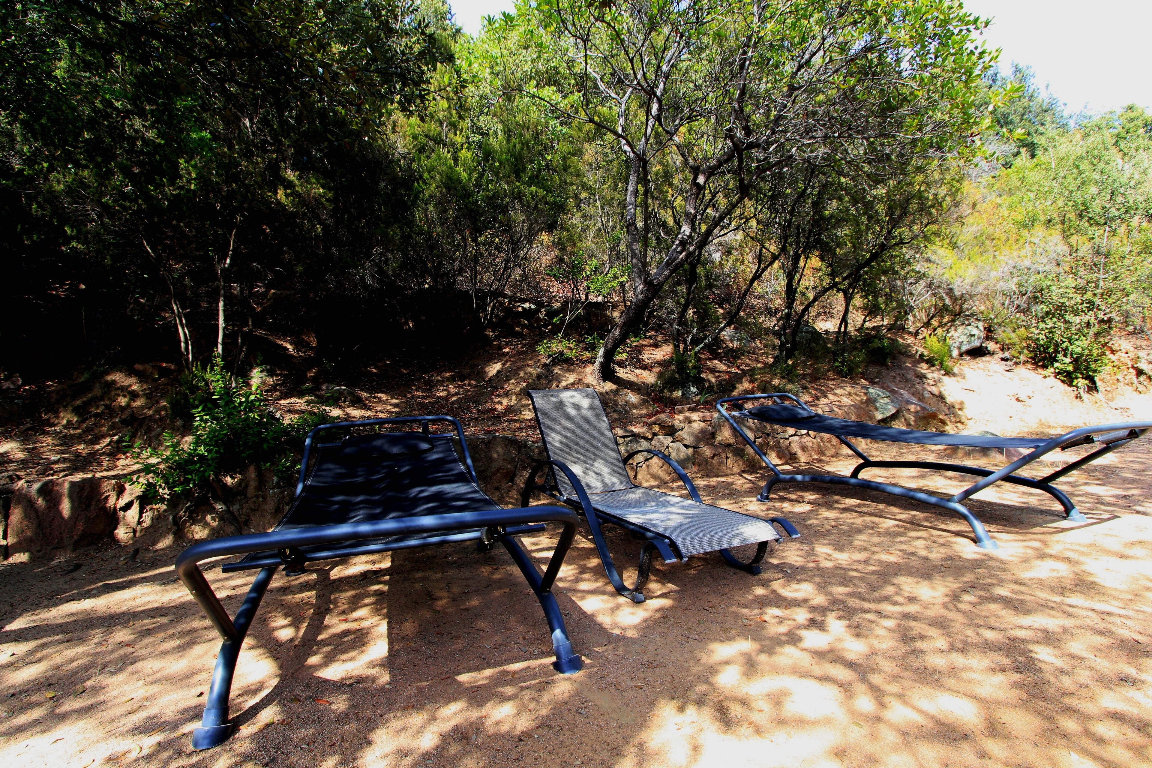 Dos sillones de metal en un área sombreada con árboles y un sendero de tierra.