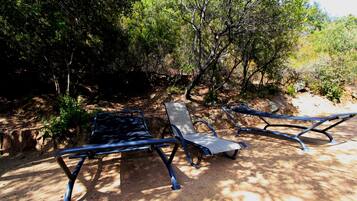 Dos sillones de metal en un área sombreada con árboles y un sendero de tierra.