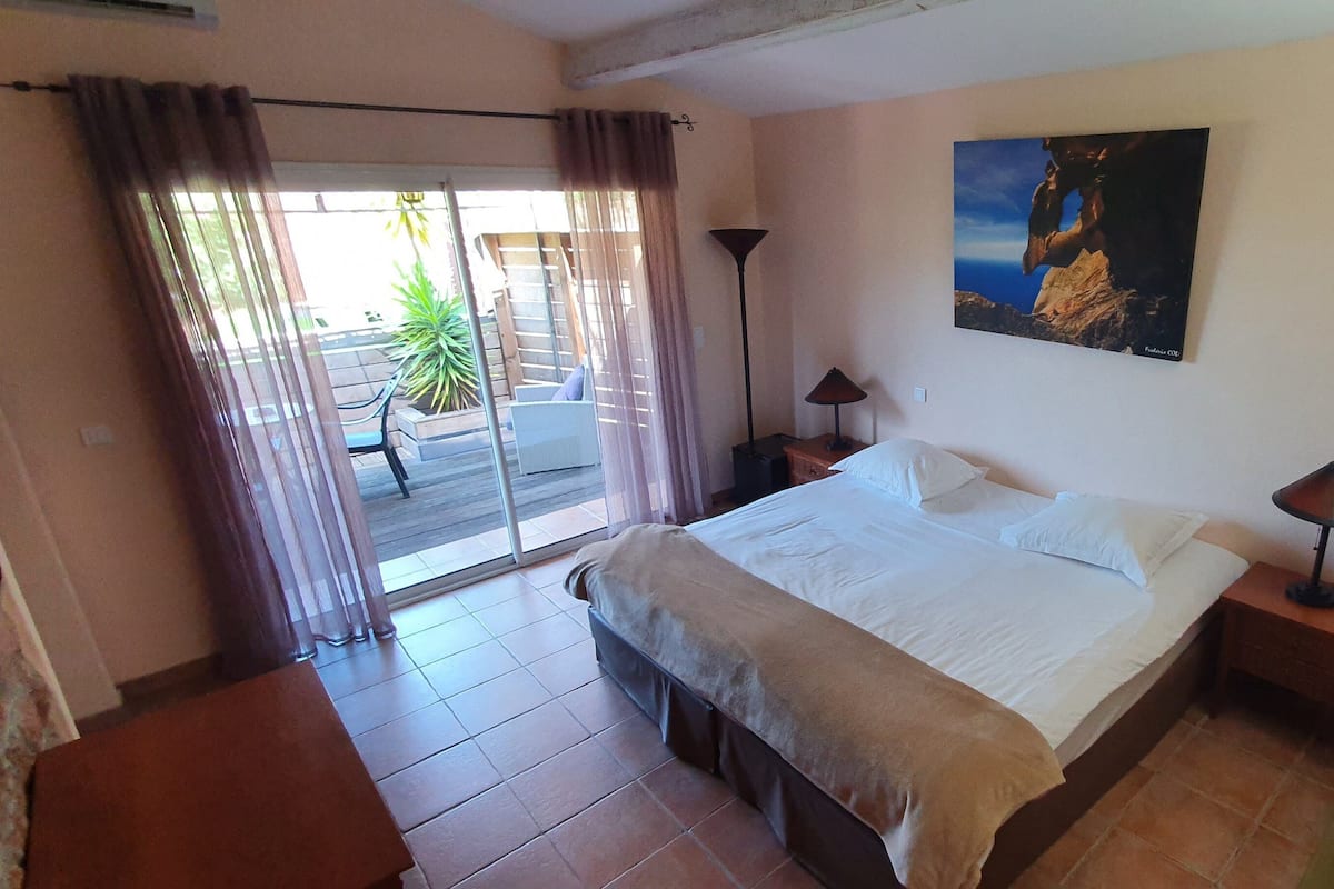 Habitación de hotel con cama, escritorio, silla, lámpara, un cuadro y vistas al exterior.
