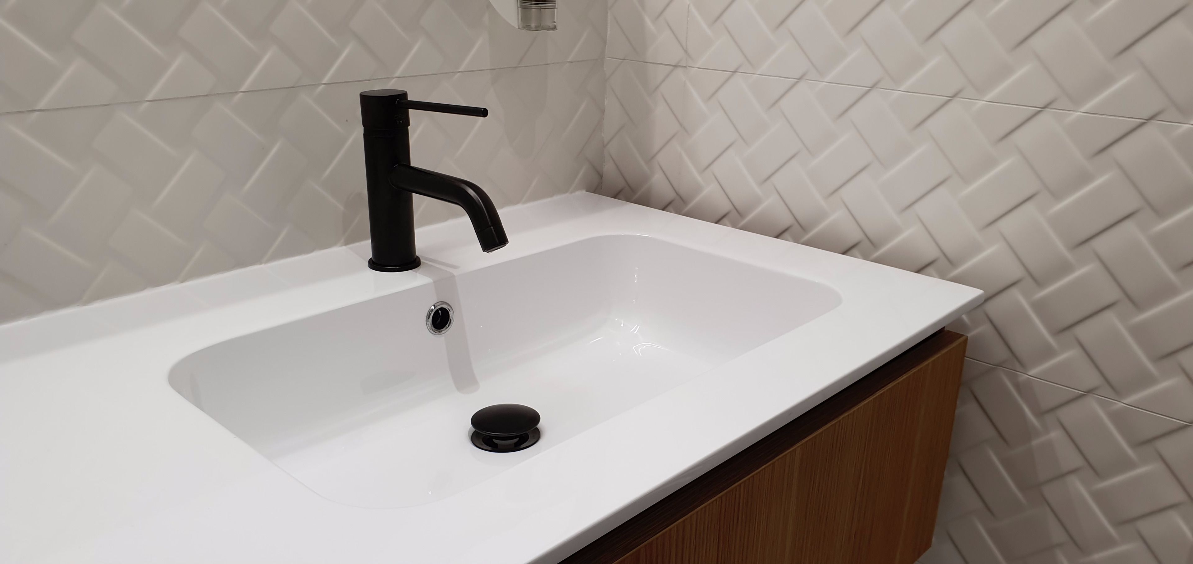 A modern bathroom with a white sink, black faucet, and a diamond-patterned tiled wall.